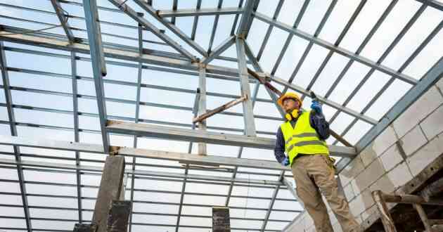 A construction worker erecting steel roof trusses of a residential building.